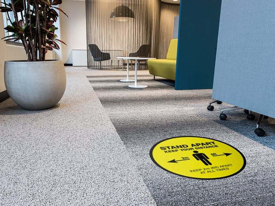Social Distancing Sticker for Carpet Tiles that says "Stand Apart Keep Your Distance" in an office