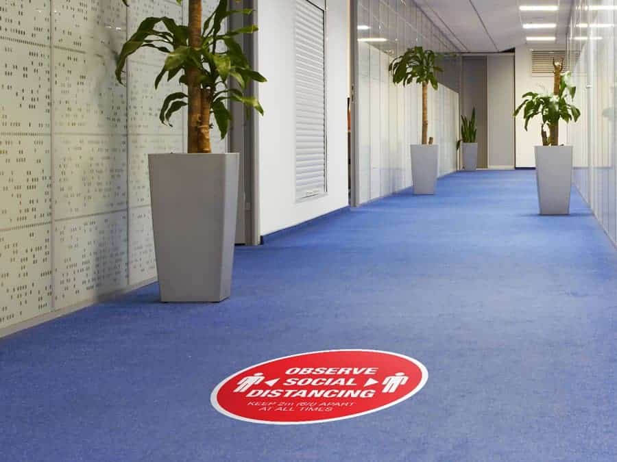 Social Distancing Sticker for Carpet Tiles that says "Observe Social Distancing" in an office hallway