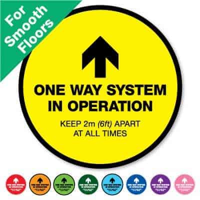 Round yellow Social Distancing Sticker for smooth floors that says "One Way System in Operation" on the top plus 8 other colours o the bottom