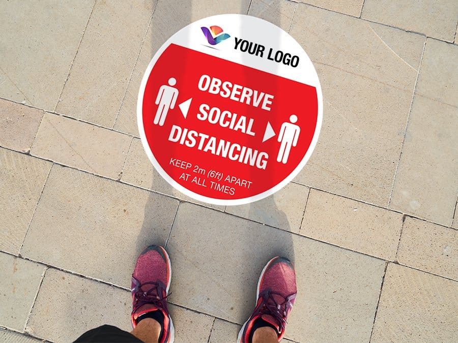 Social Distancing Floor Stickers with logo for outdoor usage "Observe Social Distancing", round Social Distancing Sticker branded with logo for outdoor usage that says "Observe Social Distancing" on a paved ground